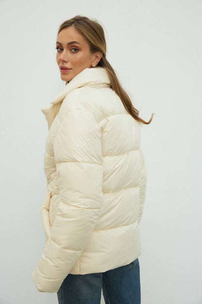 Woman wearing a cream puffer jacket against a white background