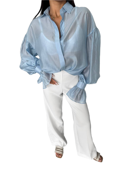 Person wearing a light blue sheer blouse with white pants on a white background