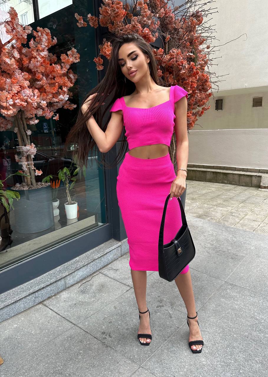Woman in a bright pink outfit standing outdoors near a building entrance.