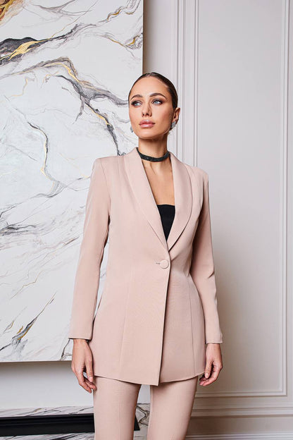 Woman wearing a light pink suit standing against a marble wall.