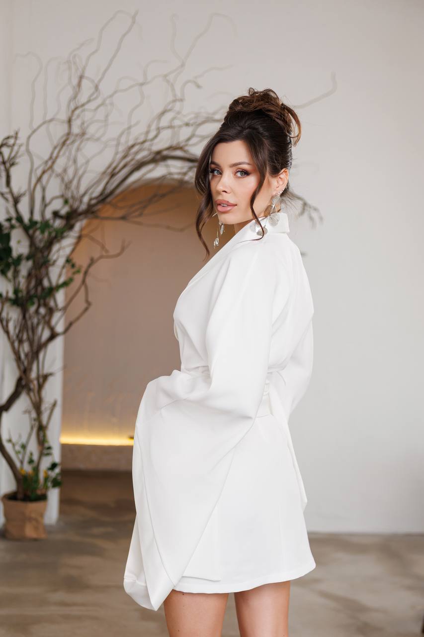 Woman in a white robe standing in a softly lit room with decorative plants.