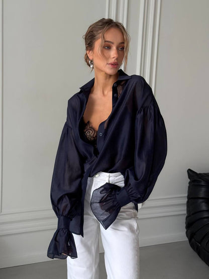 Woman wearing a dark blue oversized shirt with white pants in a minimalistic setting