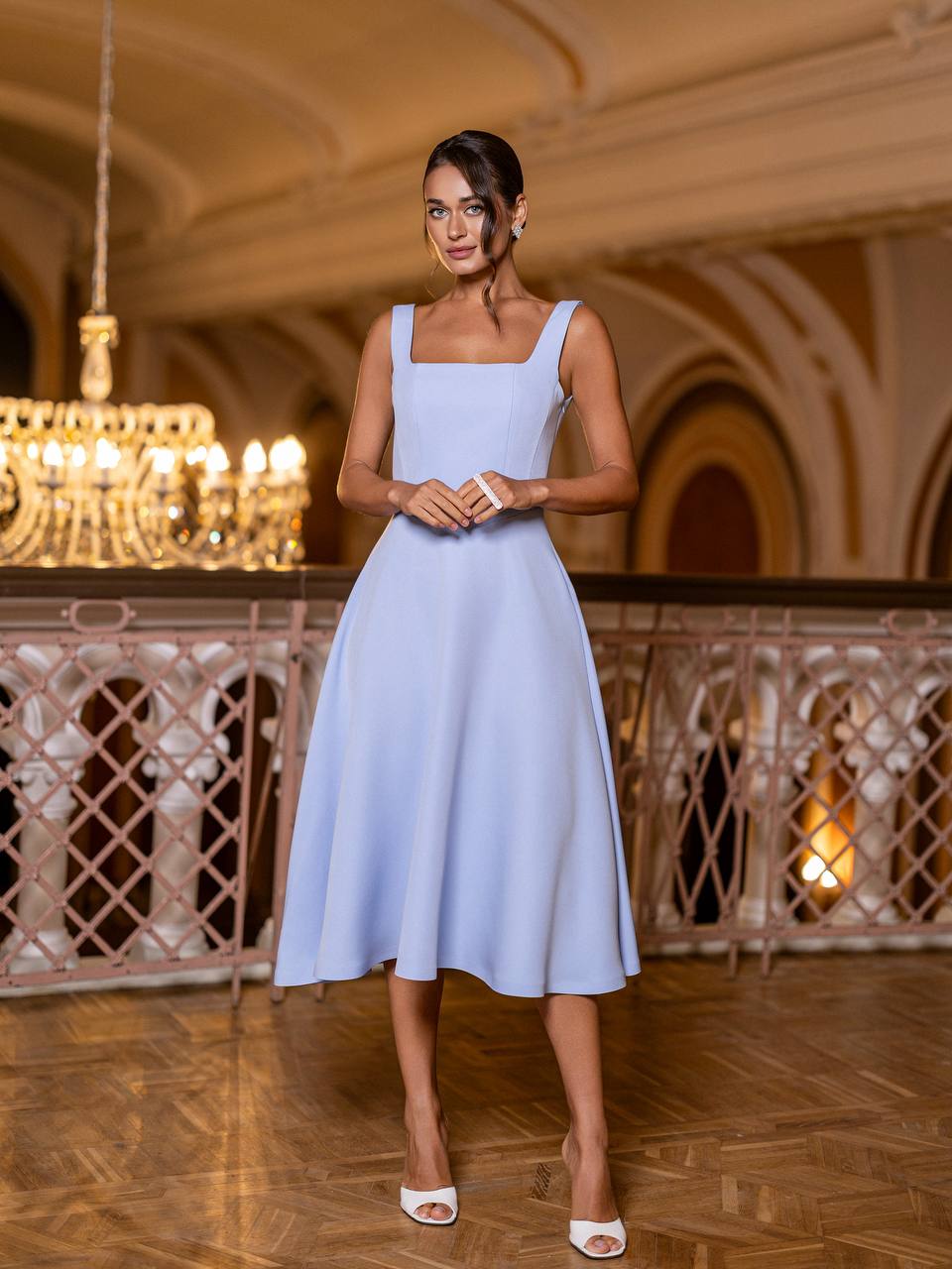 Woman in a light blue dress standing in an elegant indoor setting with chandeliers.