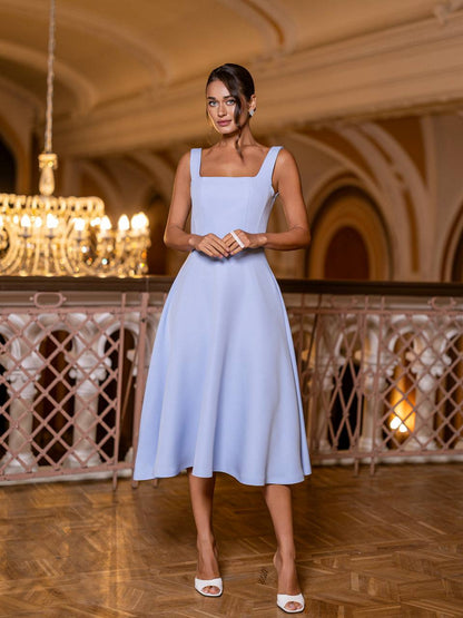 Woman in a light blue dress standing in an elegant indoor setting with chandeliers.