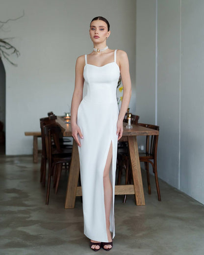 Woman in a white dress standing in a room with wooden furniture.
