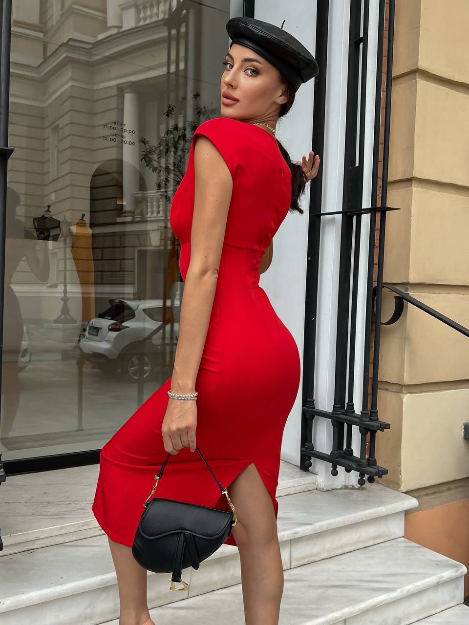 Woman in a red dress and black beret standing on steps outside a building.