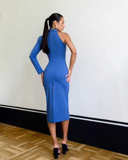 Woman wearing a blue one-shoulder dress standing against a white wall.