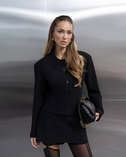 Woman in a black outfit holding a handbag against a metallic background