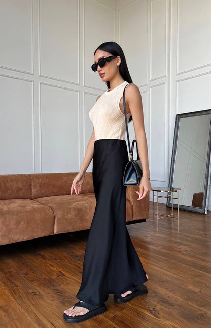 Woman in a stylish outfit with a cream top and black pants standing in a modern room.