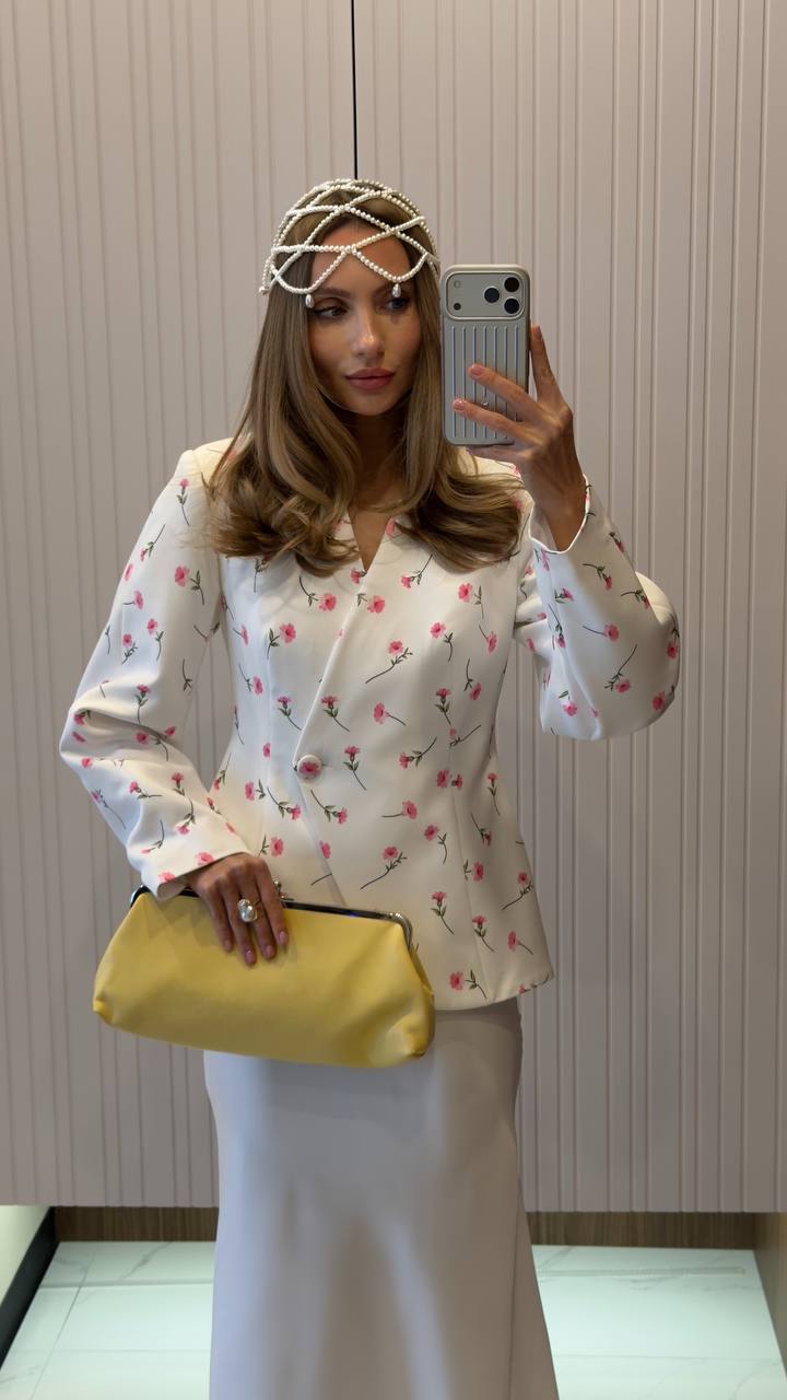 Woman taking a mirror selfie wearing a floral blouse and holding a yellow clutch.