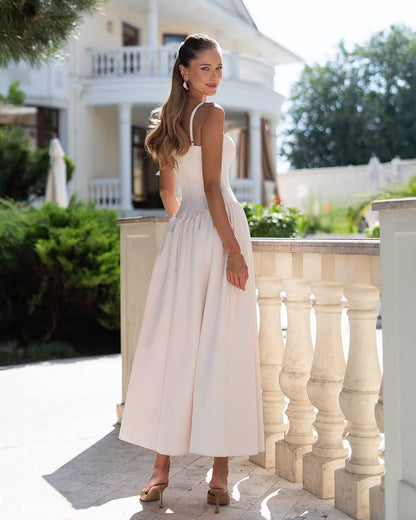 Woman in a white dress standing on a balcony with a house and garden in the background