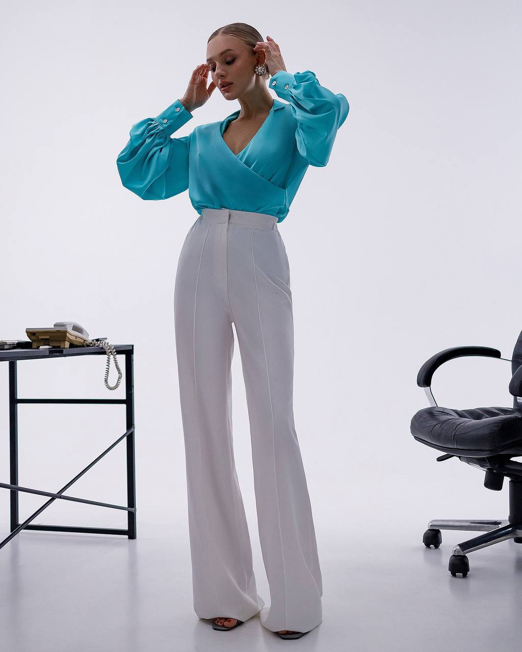 Woman in a blue top and white pants standing in an office setting.