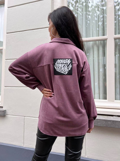 Person wearing a purple jacket with a visible brand logo, standing in front of a window.