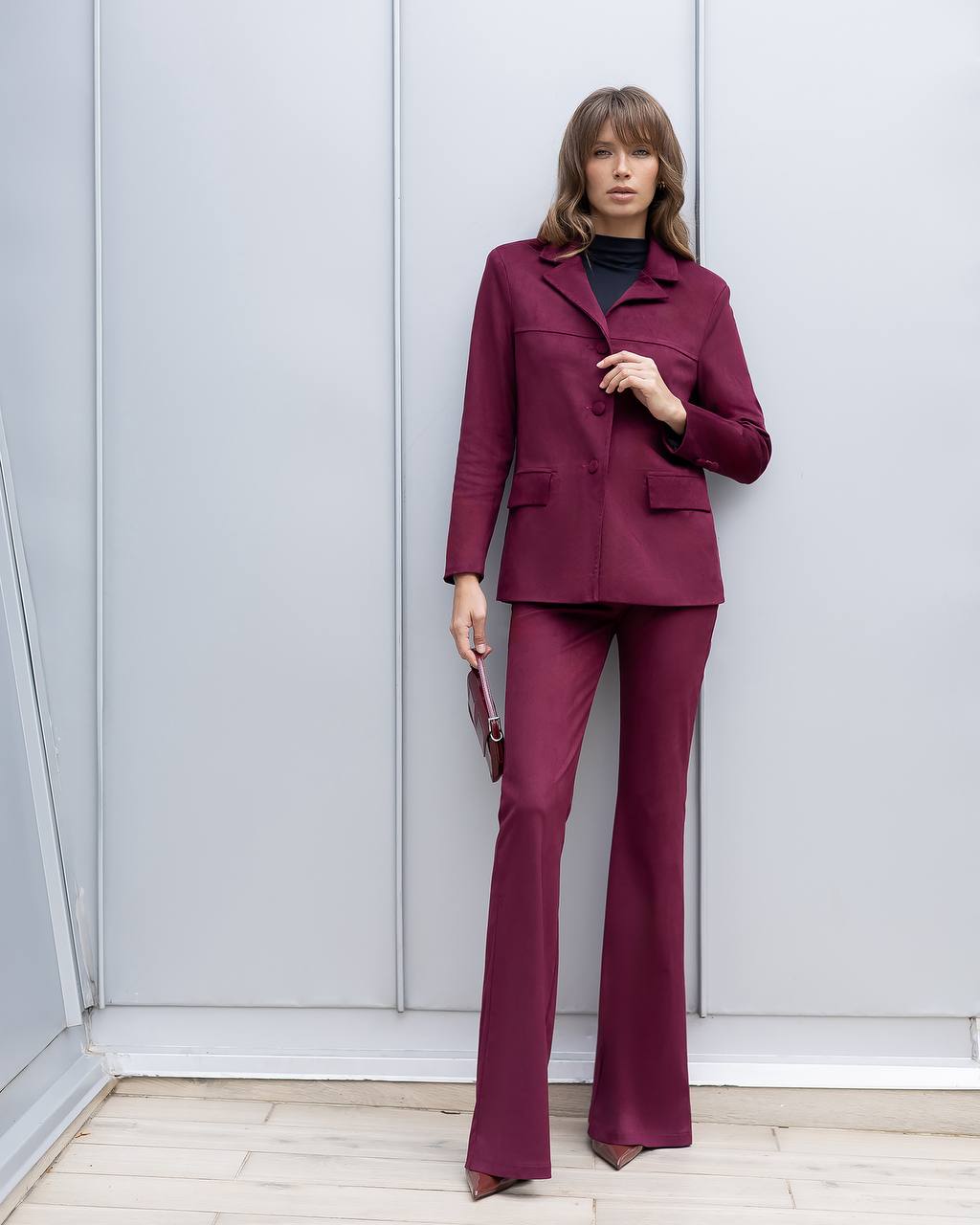 Woman wearing a burgundy suit standing against a light gray wall.