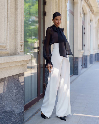 Woman in a stylish outfit with a black top and white pants standing on a sidewalk.