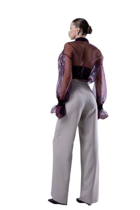 Person wearing a patterned blouse and light gray pants on a white background