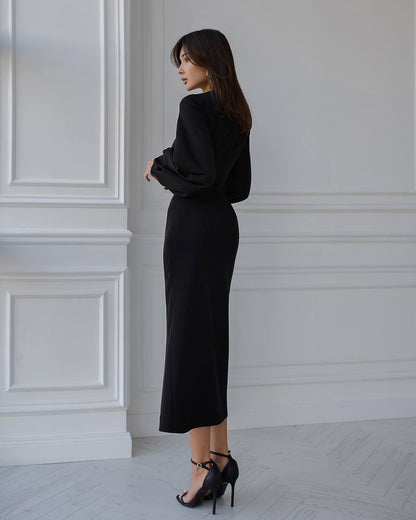 Woman wearing a black dress standing against a white wall.