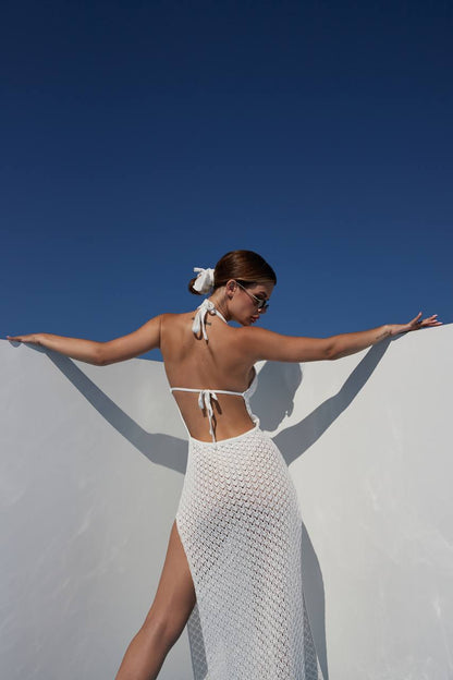 Woman in a white crochet dress standing against a blue sky