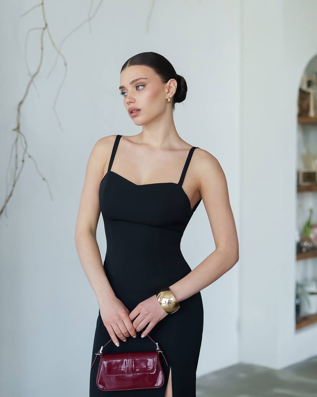 Woman in a black dress holding a red handbag against a neutral background