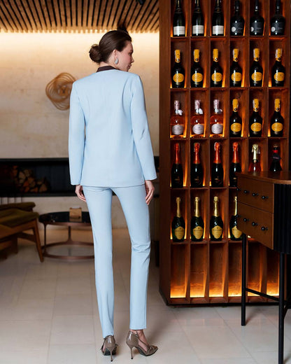 Woman in a light blue suit standing in front of a wine rack with bottles.