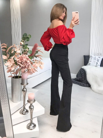 Woman taking a mirror selfie wearing a red top and black pants in a living room.