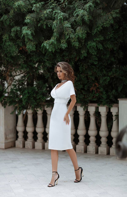 Woman in a white dress standing outdoors with greenery in the background