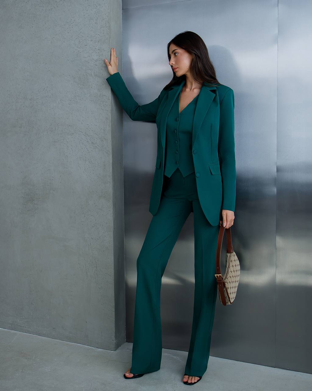 Woman in a teal suit standing against a gray wall