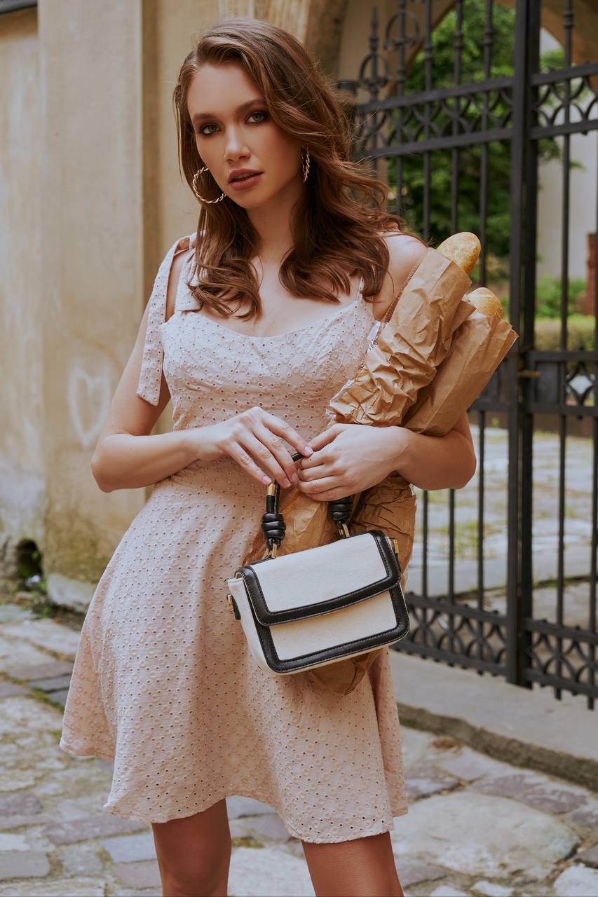Woman in a beige dress holding a large bread loaf and a handbag on a stone path.