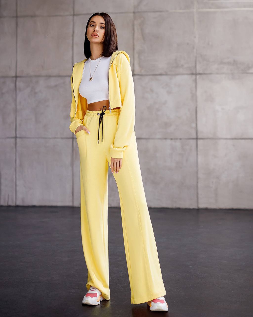 Woman in a yellow outfit standing against a gray concrete wall.