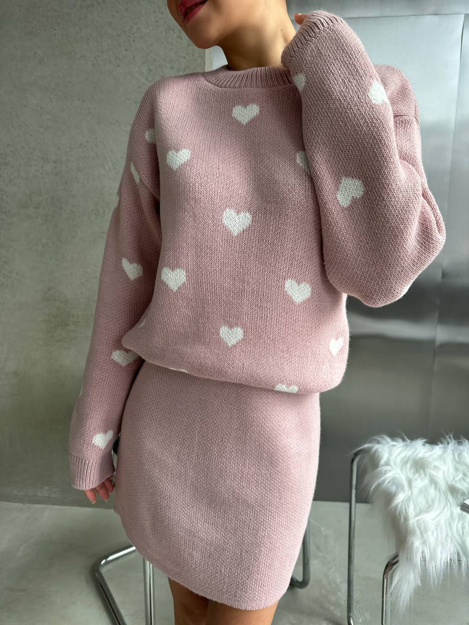 Pink knit outfit with heart patterns on a neutral background