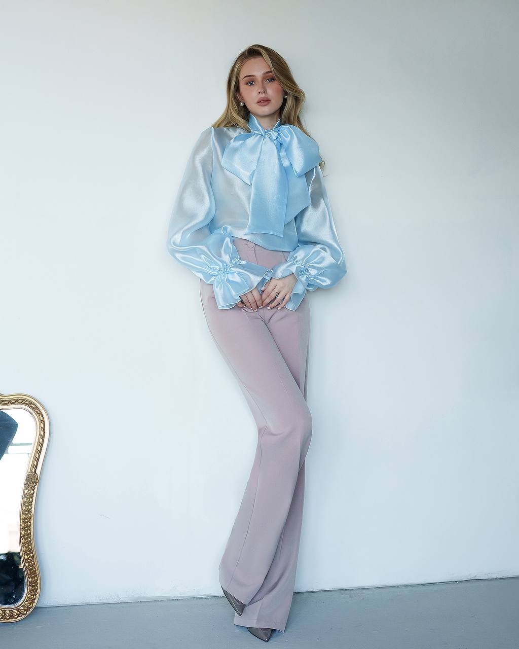 Person wearing a light blue blouse and pink pants against a white wall.