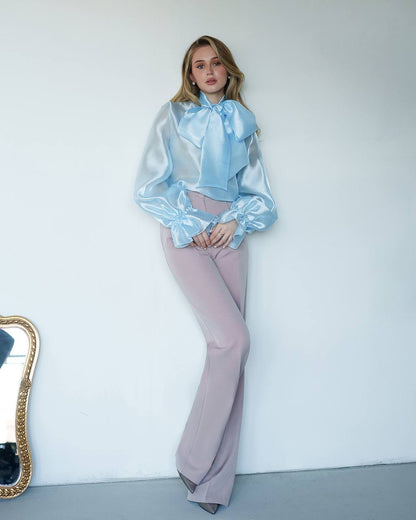 Person wearing a light blue blouse and pink pants against a white wall.