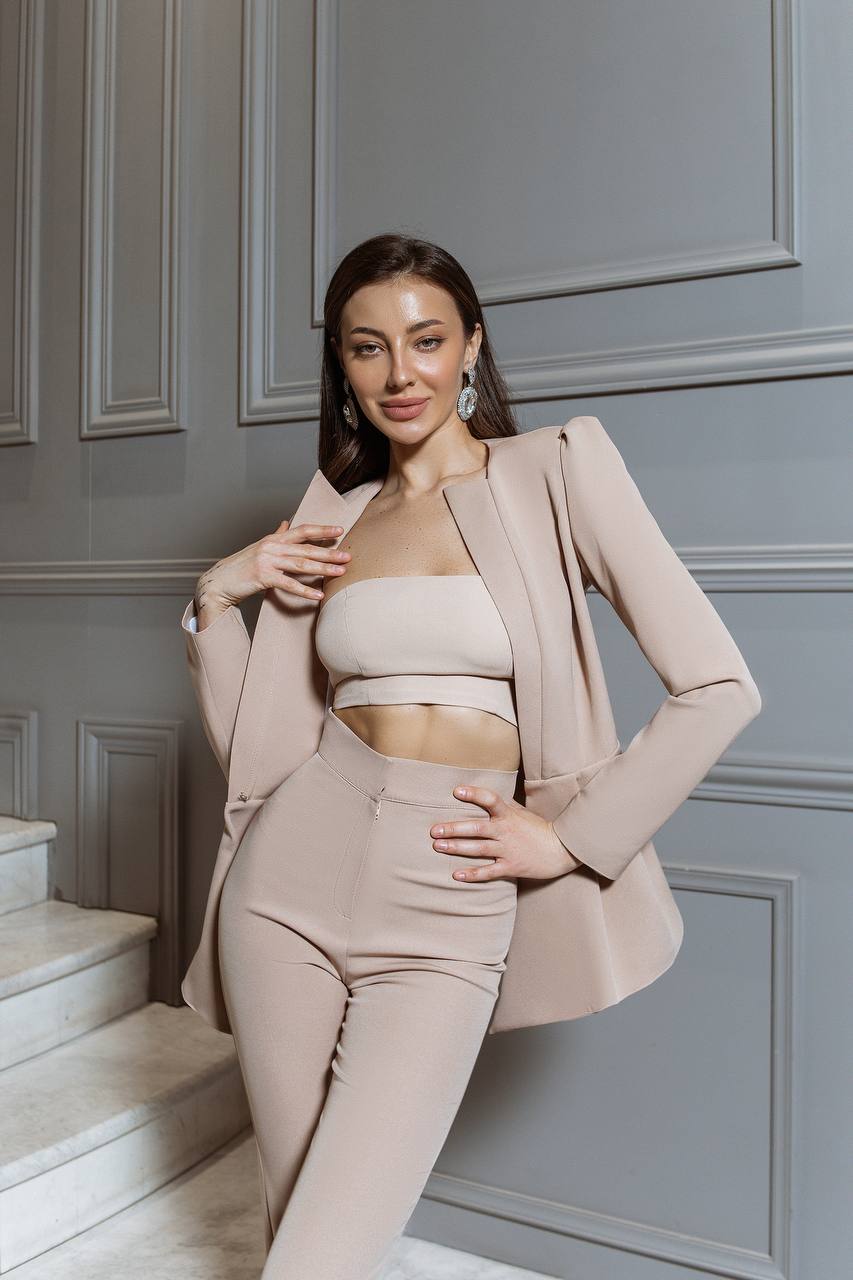 Woman in a beige outfit posing against a gray paneled wall.