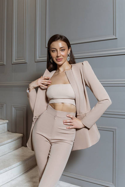Woman in a beige outfit posing against a gray paneled wall.