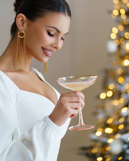 Woman holding a cocktail glass in front of a decorated Christmas tree