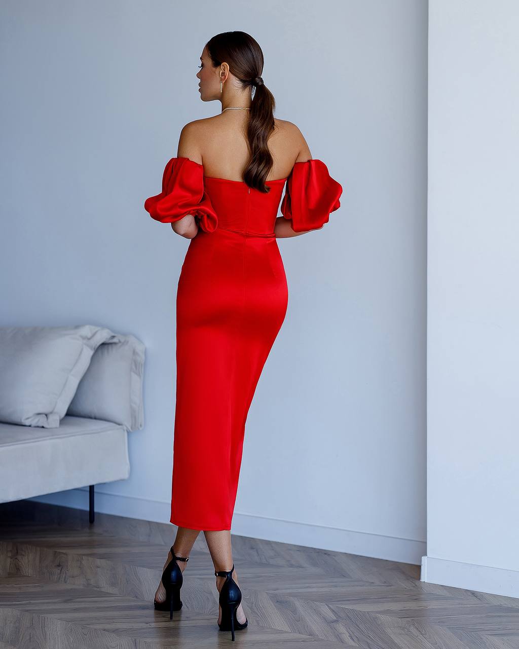 Woman wearing a red off-shoulder dress in a minimalistic room.