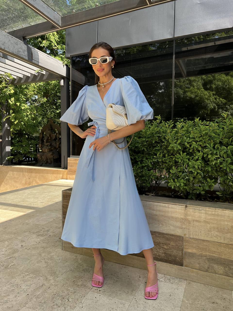 Woman in a light blue dress standing outdoors with greenery in the background