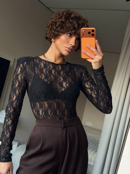 Woman taking a mirror selfie wearing a black lace top and brown pants.