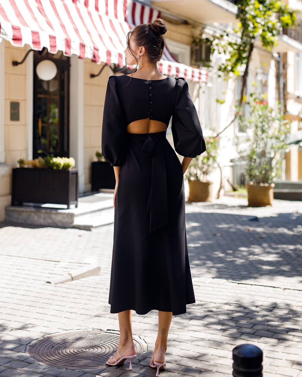 Woman wearing a black dress with cut-out back standing on a street.