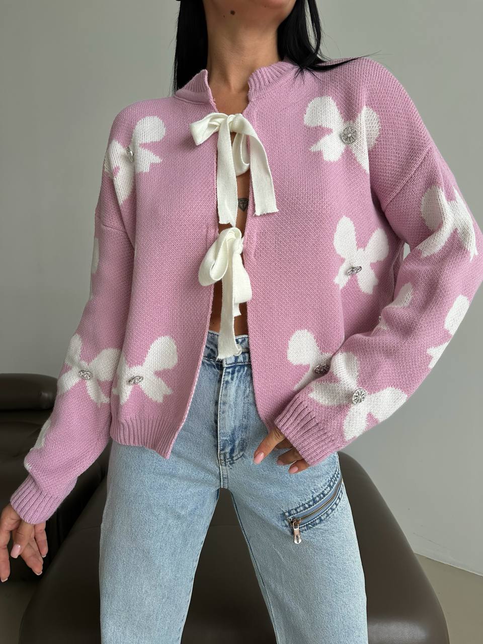Person wearing a pink sweater with white floral patterns and light blue jeans.