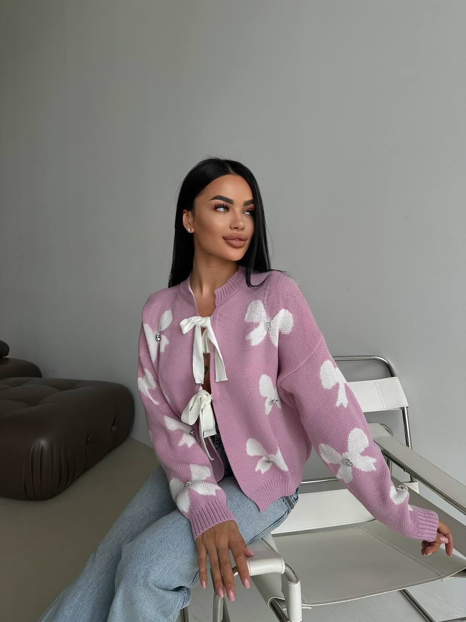 Woman wearing a pink sweater with white patterns sitting on a chair.