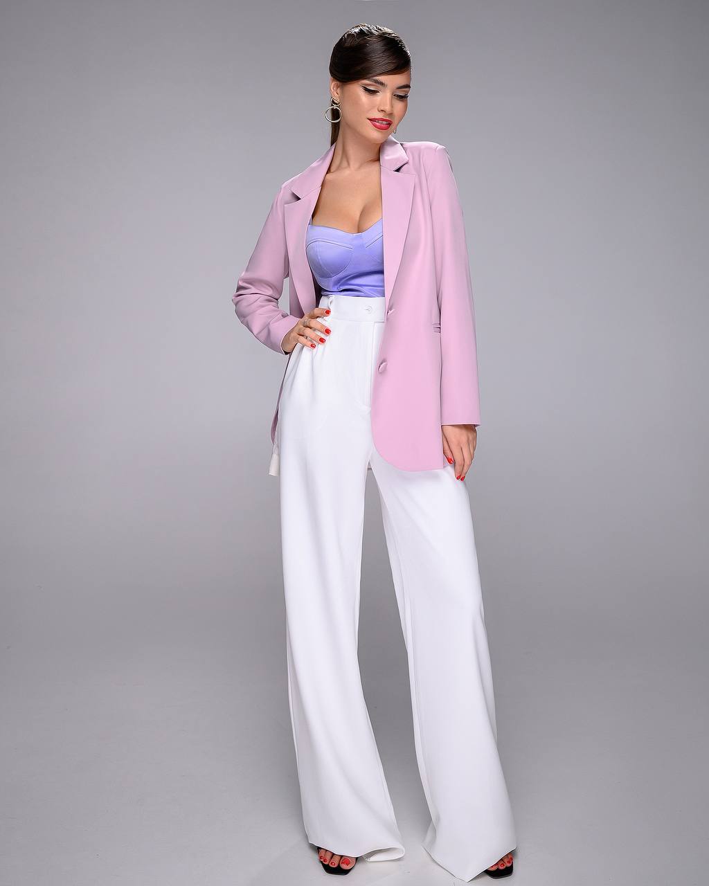 Woman wearing a pink blazer, purple top, and white pants on a gray background