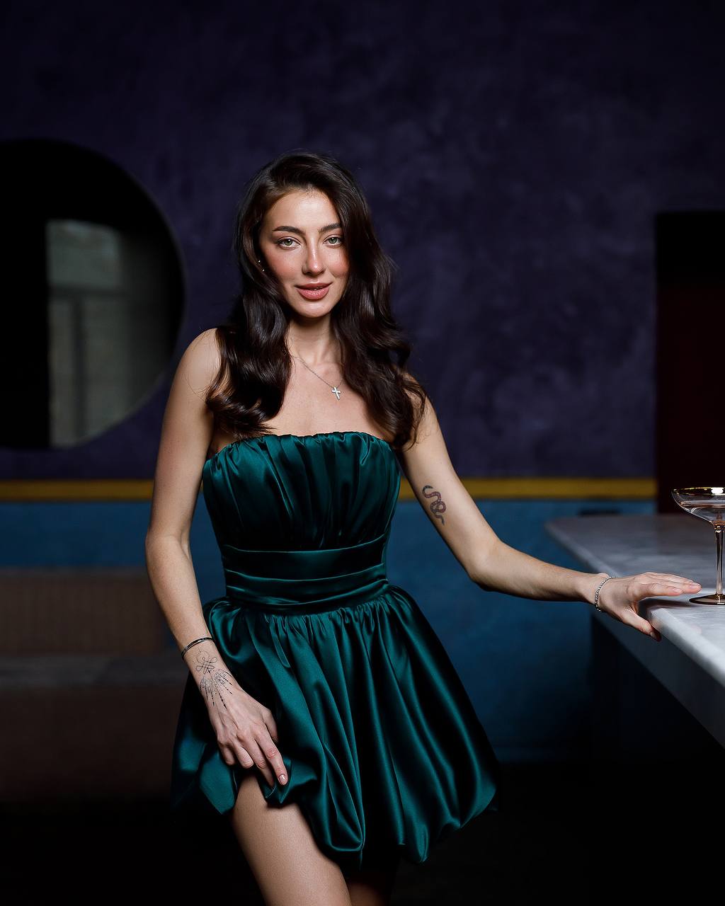 Woman in a green dress sitting at a bar counter with a dark background