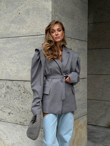 Woman wearing a gray blazer and light blue jeans against a stone wall.