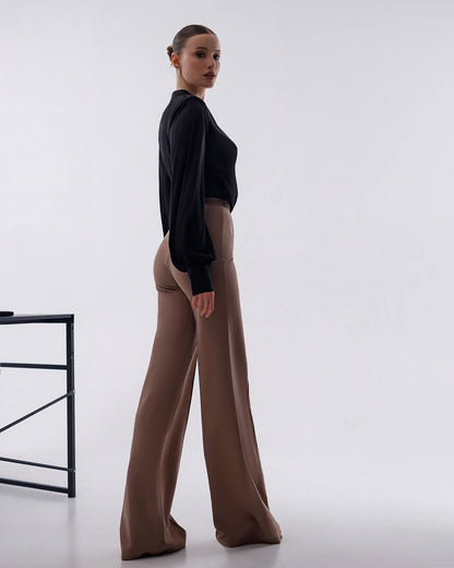 Woman wearing a black top and brown pants on a white background