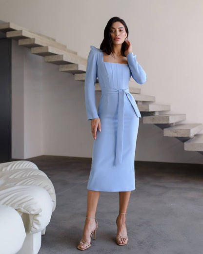 Woman in a light blue dress standing in a modern indoor setting with stairs.