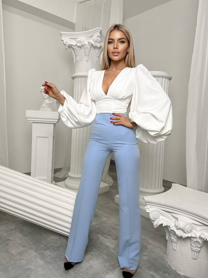 Woman in a white blouse and light blue pants standing in an elegant interior setting.