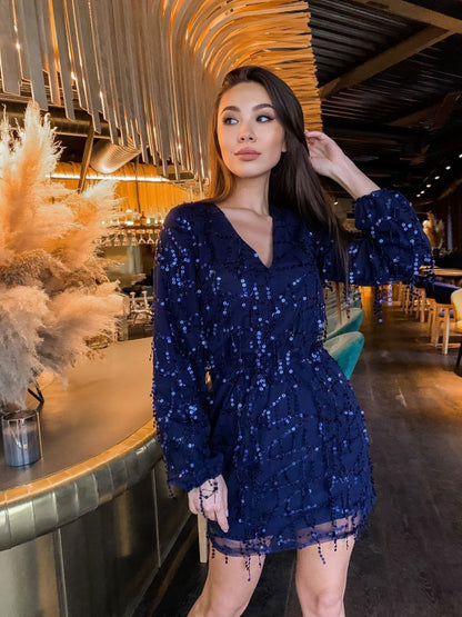 Woman in a blue sequin dress standing in a stylish indoor setting.