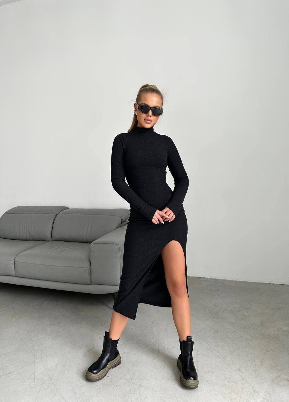 Woman wearing a black dress with a slit standing in a minimalistic room.