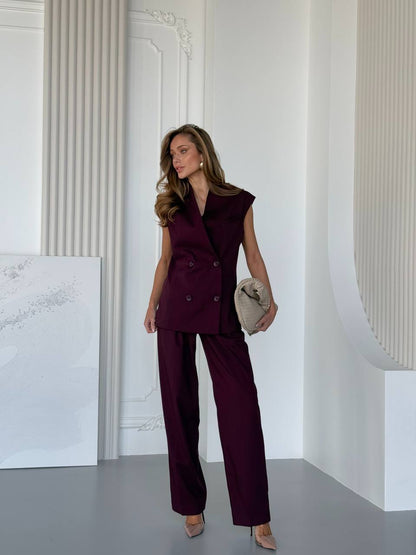 Woman in a burgundy suit standing in a minimalistic room with white walls.